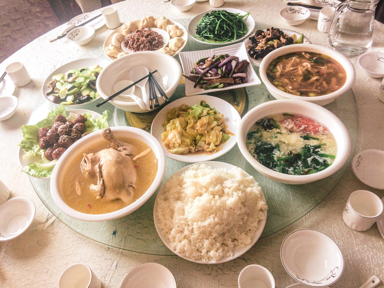 Chinese dishes on a Lazy Susan rotating table including a bowl of chicken soup with a whole chicken