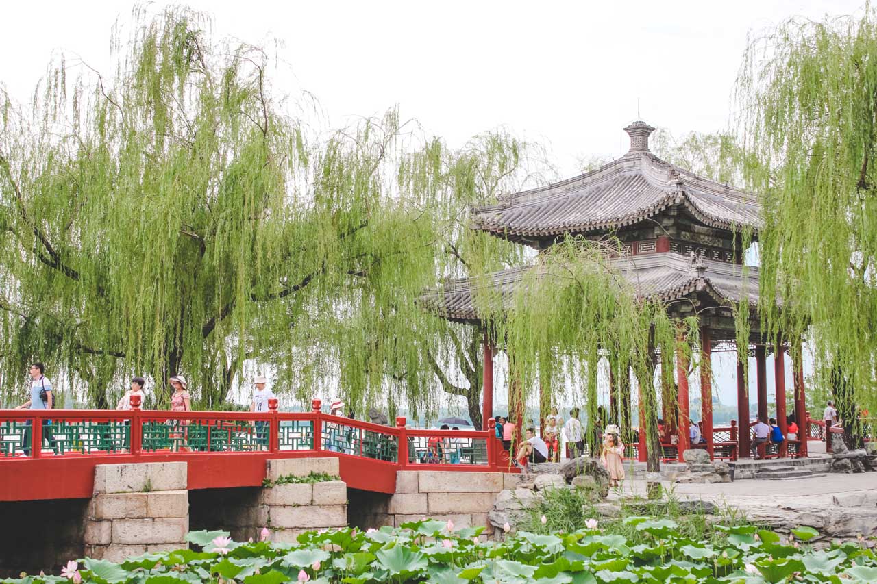A red bridge leading to a traditional Chinese pavilion surrounded by trees at the Summer Palace