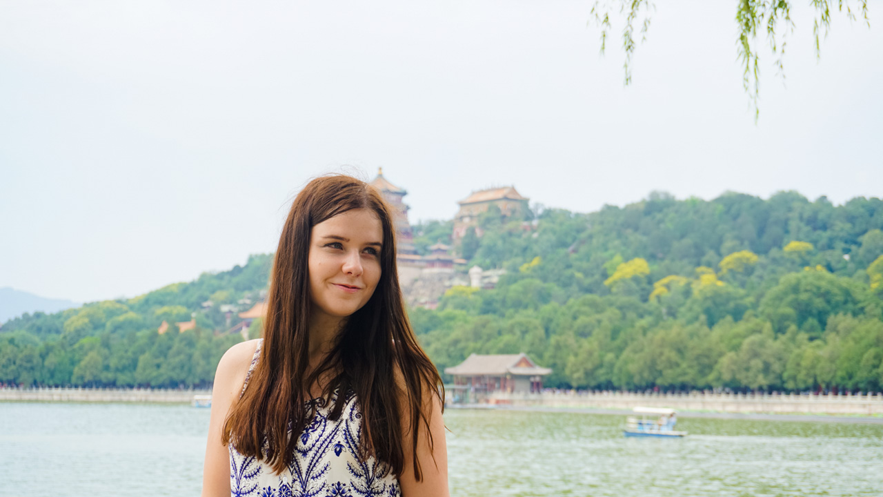 Girl in a white and blue dress looking sideways with Kunming Lake and Longevity Hill behind her