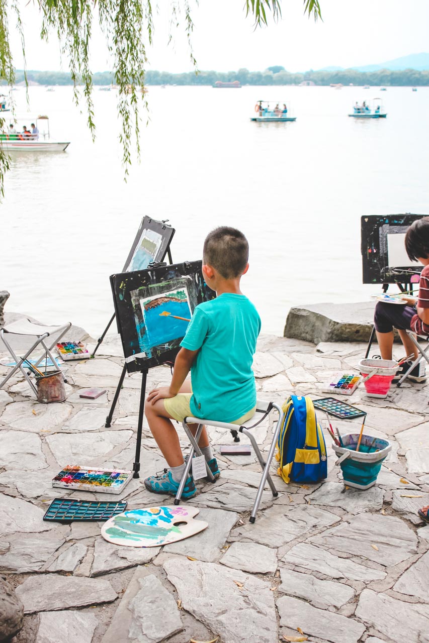 A young Chinese boy painting by the waterfront at the Summer Palace in Beijing, China
