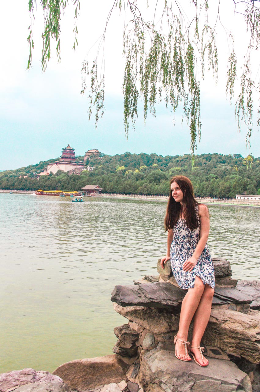 Woman in a white and blue dress sitting on a stone on the shore of Kunming Lake