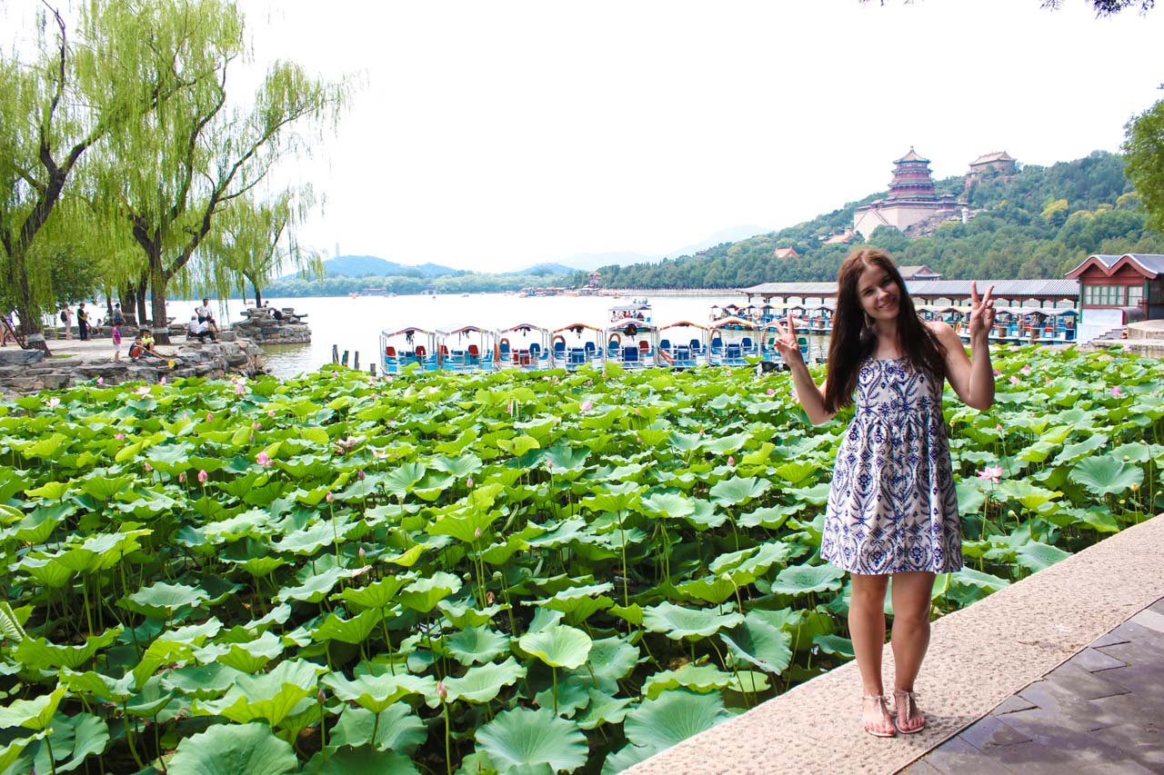 Woman throwing peace signs as she's standing on the shore of Kunming Lake at Beijing's Summer Palace