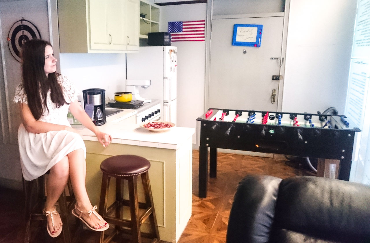 Girl in a white dress sitting on a bar stool inside a replica of Joey and Chandler's apartment