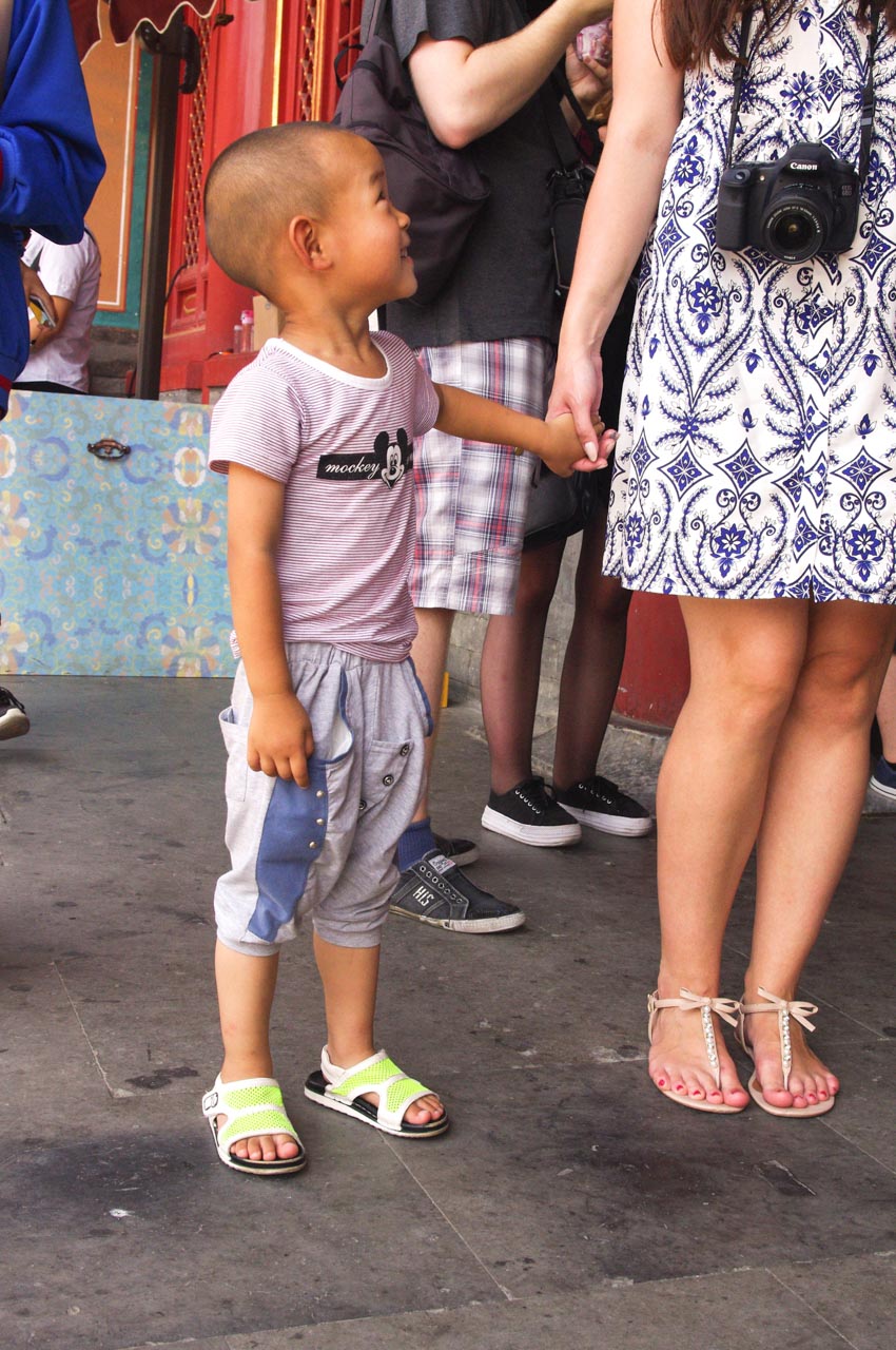 Smiling Chinese boy looking up at a woman in a white and blue dress whose hand he is holding