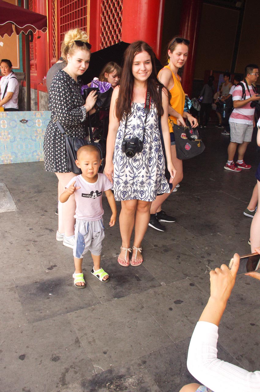 Smiling woman in a blue and white dress with a camera around her neck standing next to a Chinese boy