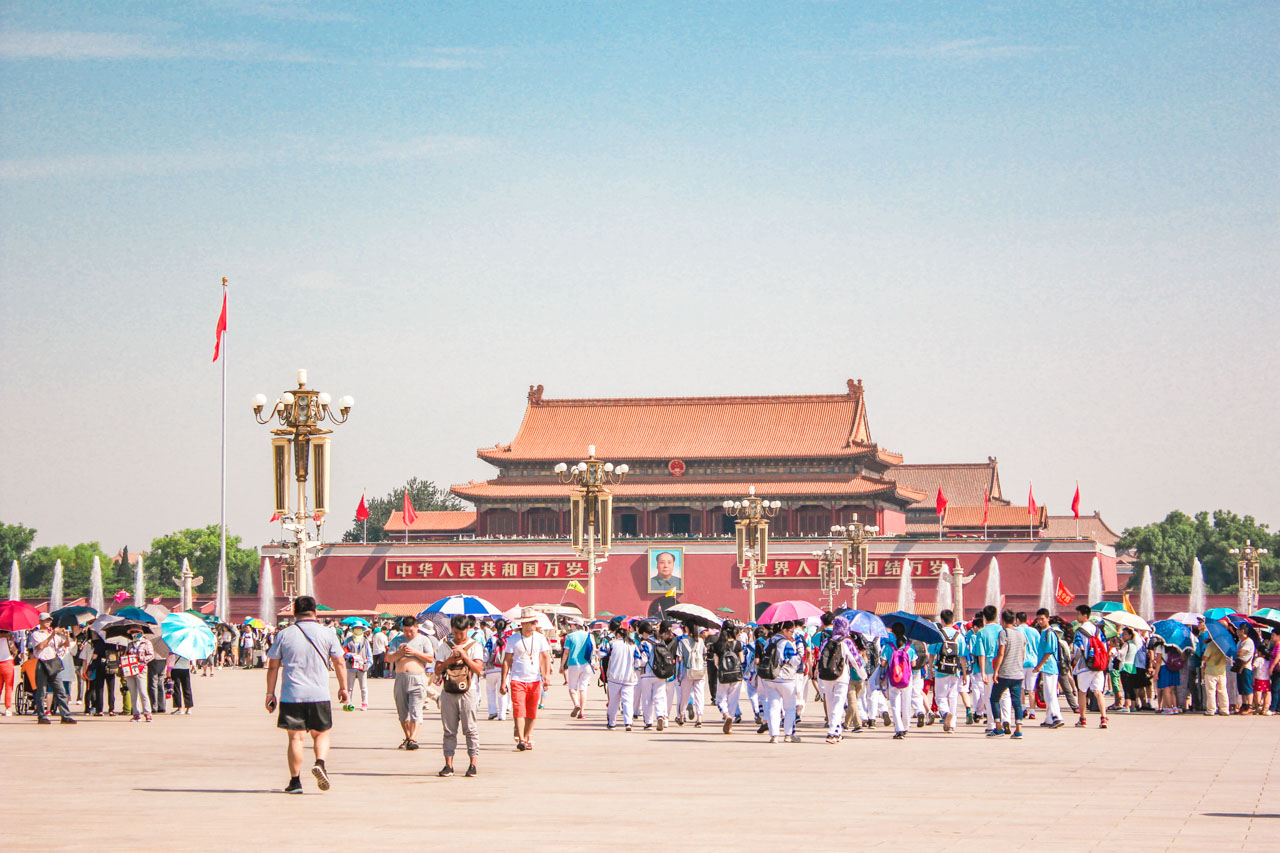 Tourists with umbrellas walking on Tiananmen Square towards the Tiananmen Gate
