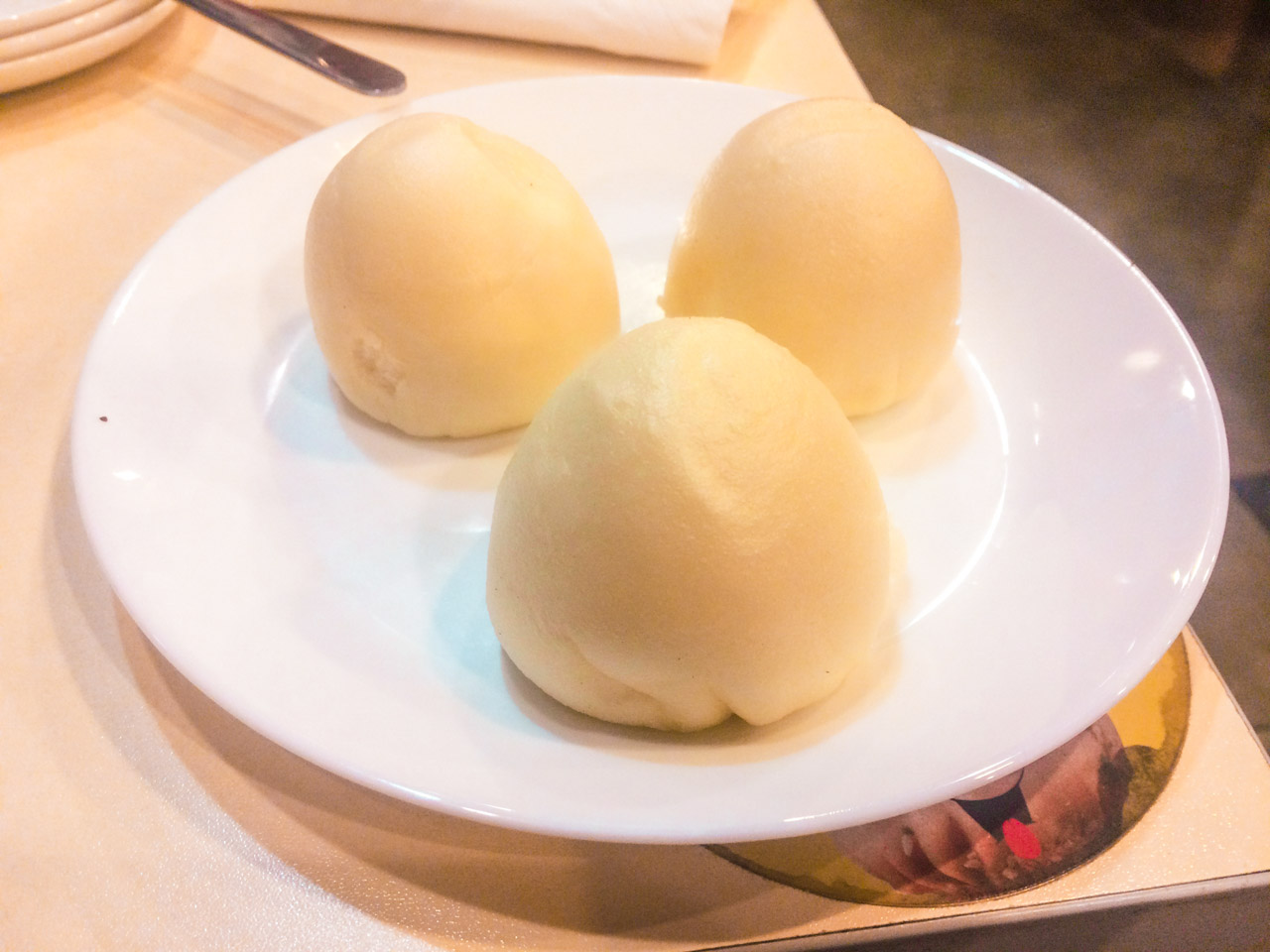 A close-up shot of three custard buns on a white plate on a wooden table at a restaurant in Beijing