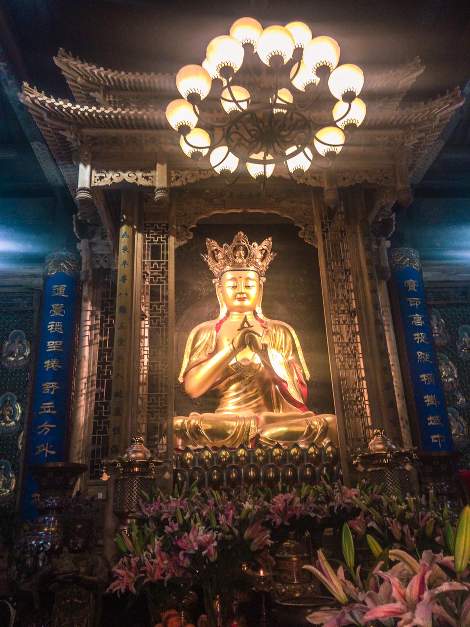 A Buddha statue with a crown on its head behind an altar at a traditional Chinese temple in Beijing