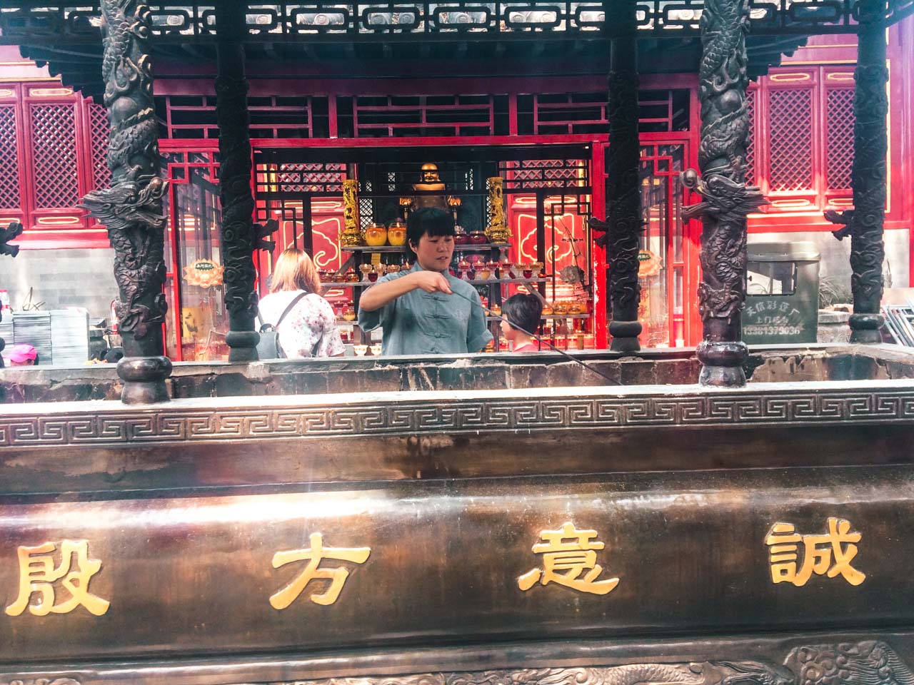 A Chinese woman burning incense sticks in front of a traditional temple in Beijing
