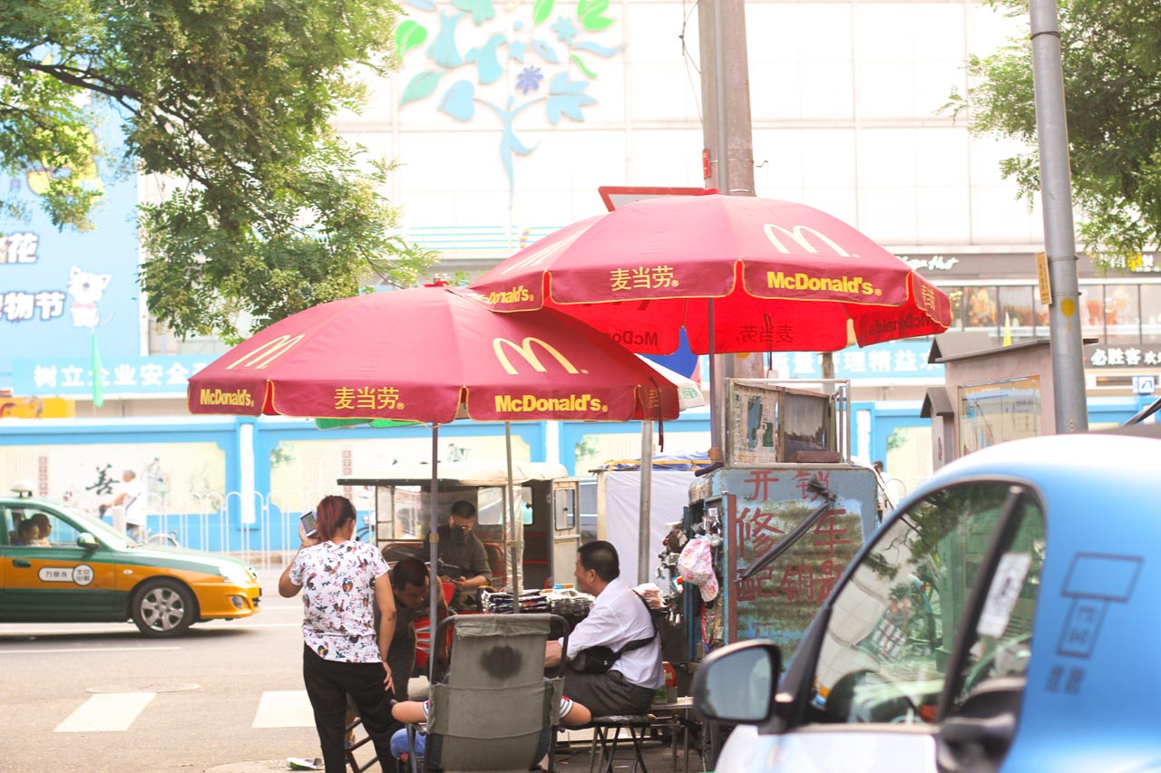 Group of Chinese street vendors sitting under red McDonald's umbrellas in a street of Beijing, China