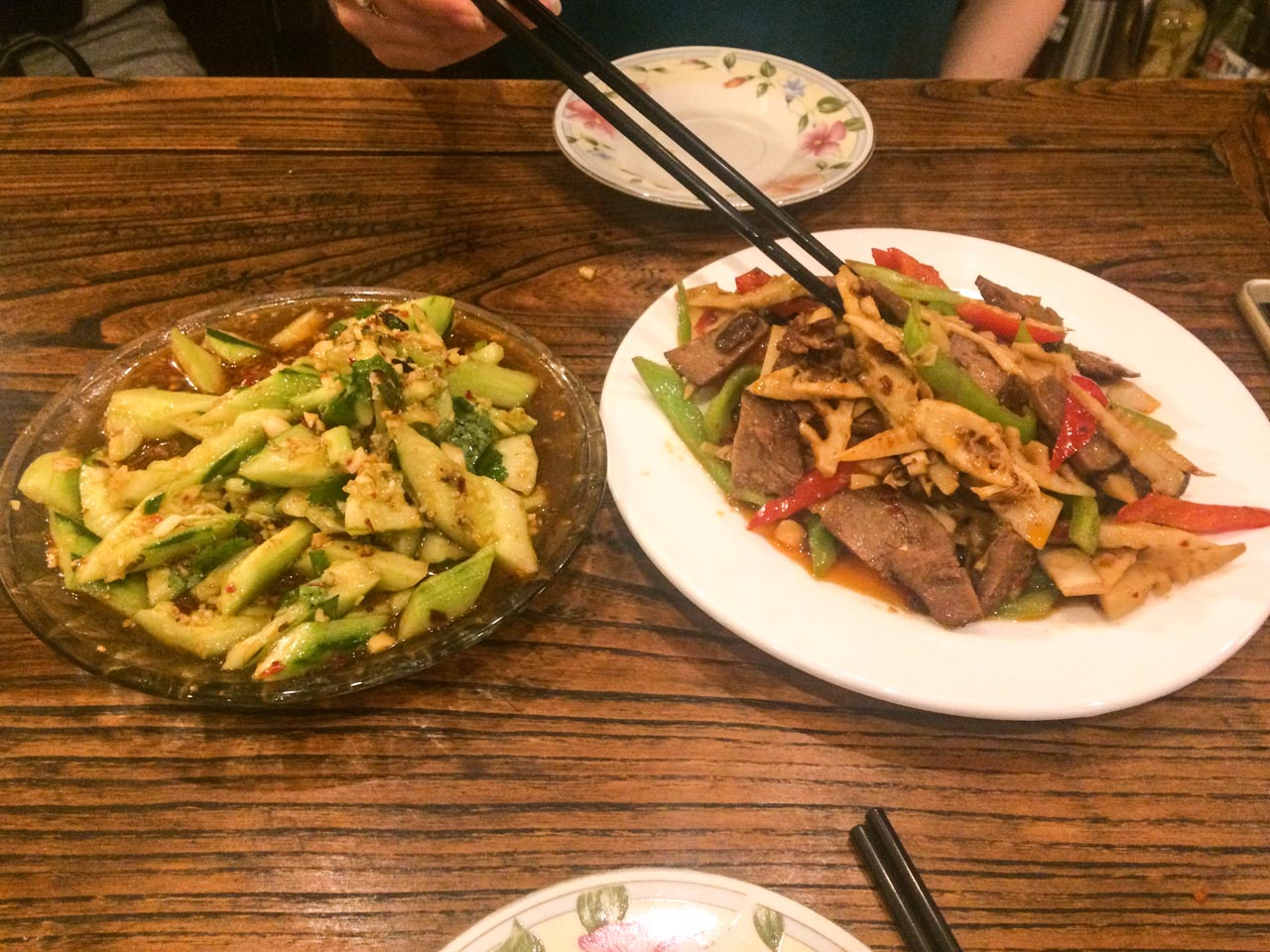 Plates with Chinese cucumber salad and beef with vegetables on a wooden table