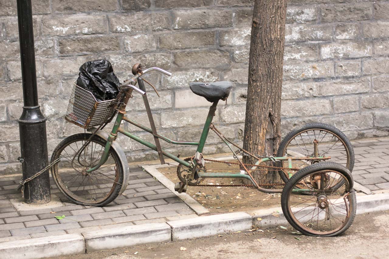 An old rusty tricycle chained to a tree in a street in Beijing, China