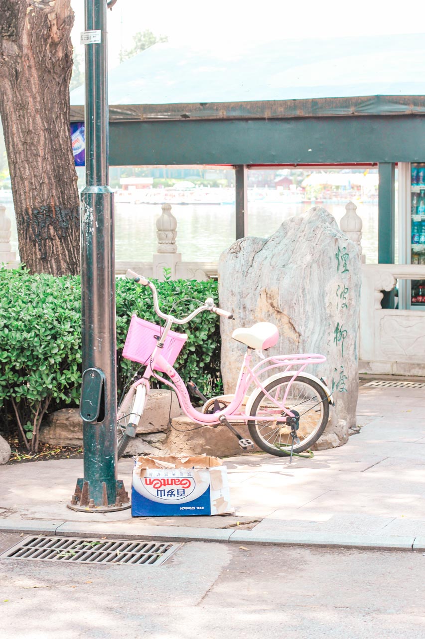 A pastel pink bike parked next to a lamp post at Houhai Park in Beijing, China