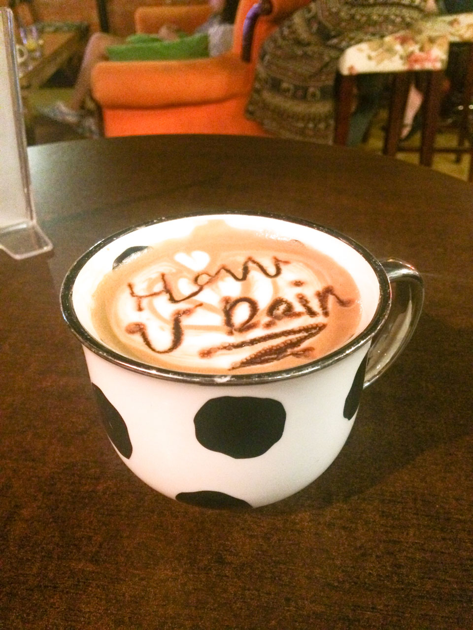 Cup of coffee with "How U Doin" written on the coffee foam on a table at the Friends Café in Beijing