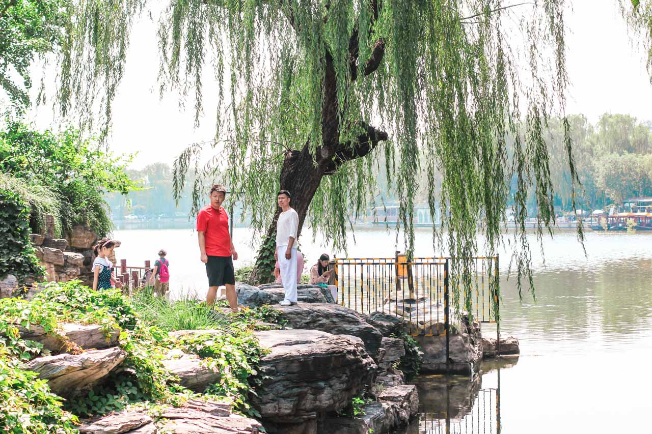 Two Chinese men standing under a tree by the edge of Huohai Lake in Beijing, China