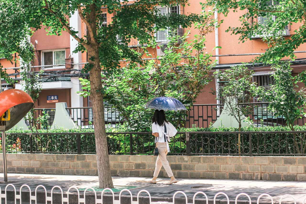Young Asian woman walking down a street in Beijing, China, carrying a blue umbrella over her head