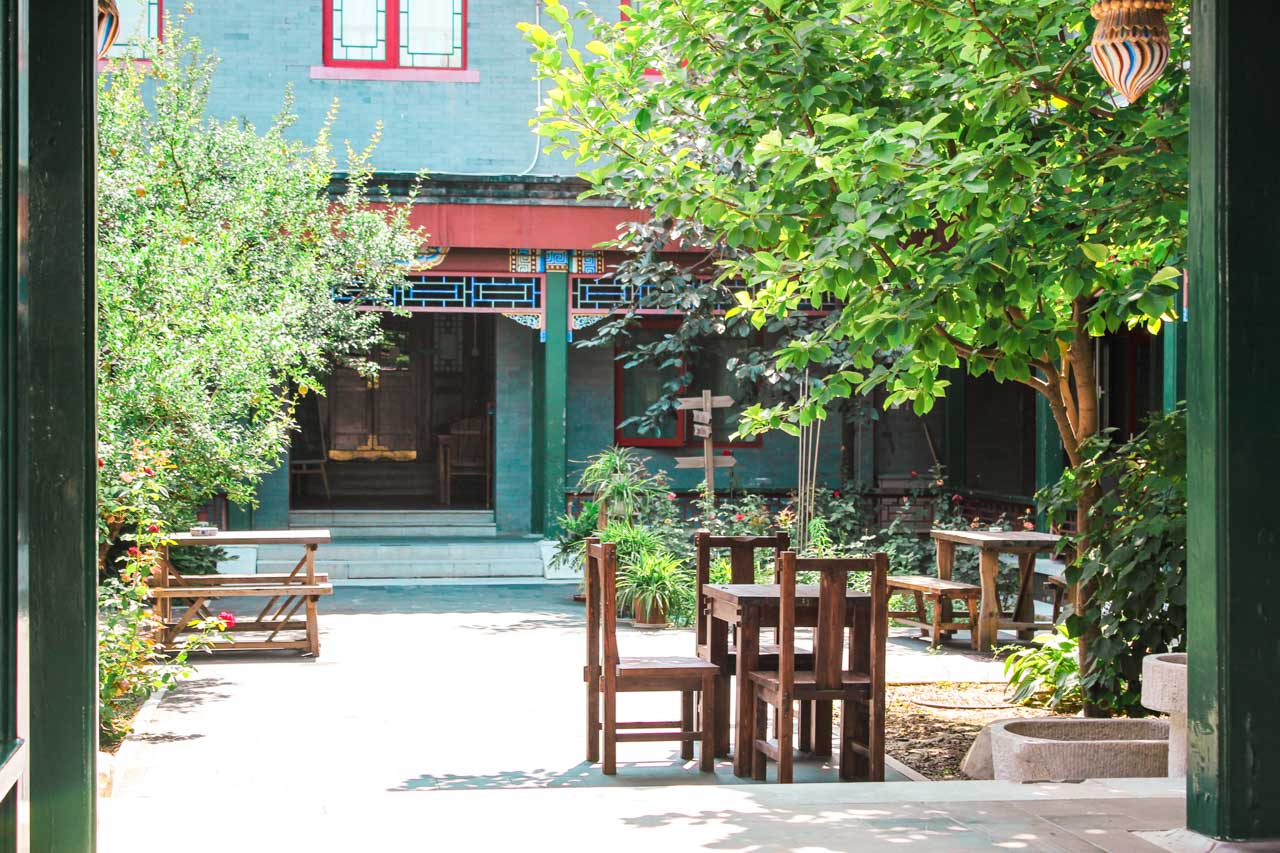 Outdoor patio area of Beijing Heyuan International Youth Hostel with trees and wooden furniture