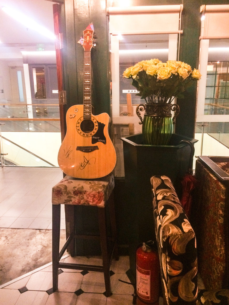A flower vase and an autographed guitar standing on a bar stool propped up against the wall