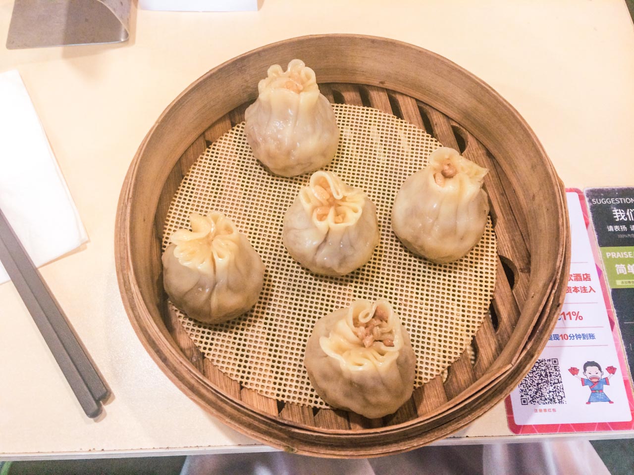 Five Xiao Long Bao dumplings in a traditional bamboo steamer placed on a wooden table
