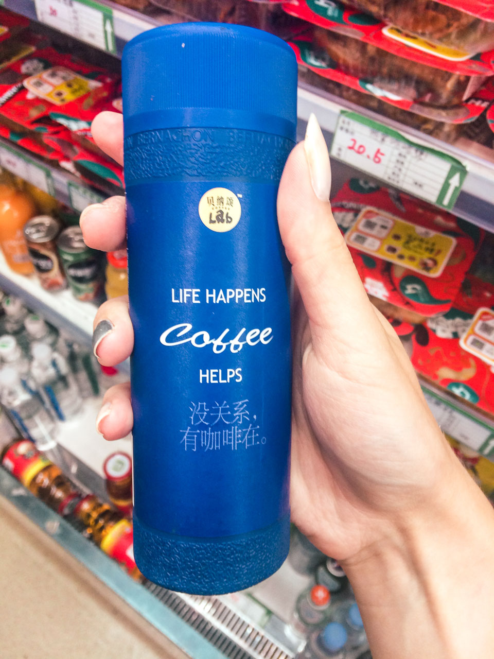Woman's hand holding a can of coffee with "Life happens, coffee helps" and Chinese translation on it