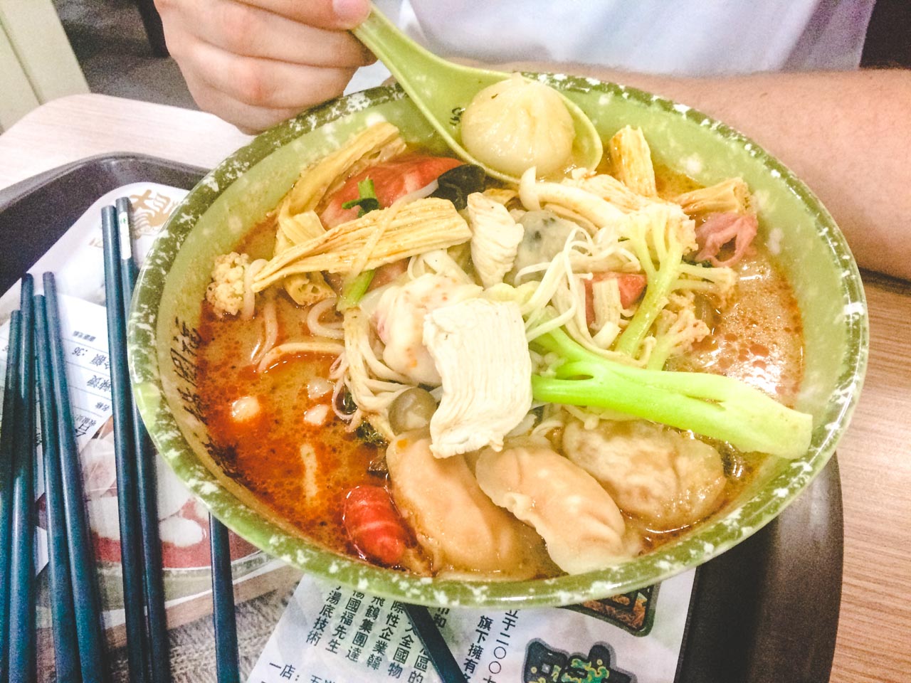 Man holding a small dumpling on his spoon above a big bowl of Asian-style soup