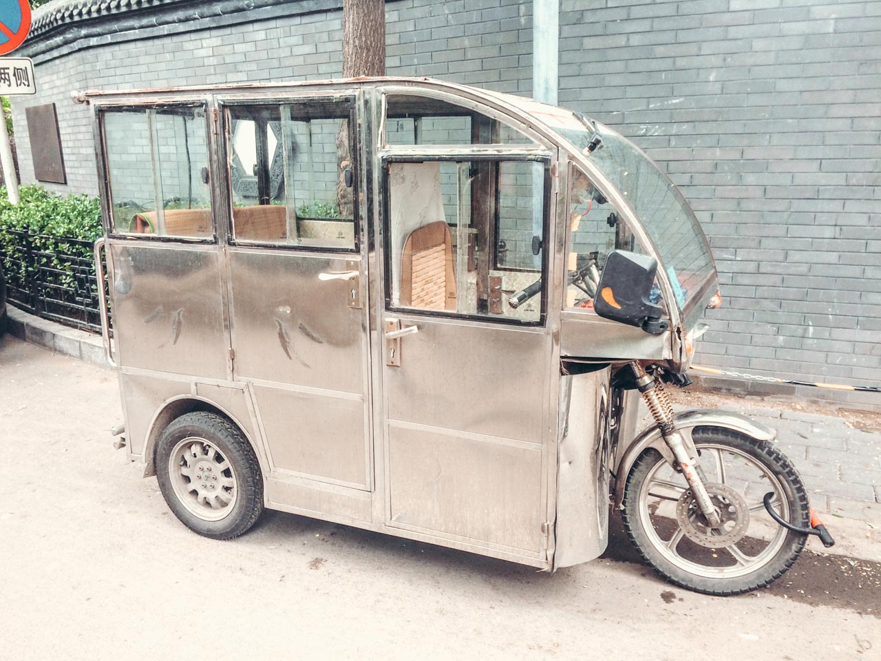 A metal vehicle resembling a rickshaw parked in a street in Beijing, China