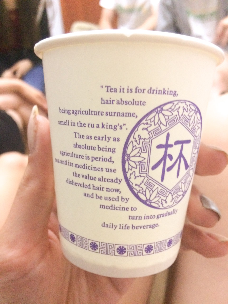 A woman's hand holding up a paper cup with a funny Chinese translation written on it
