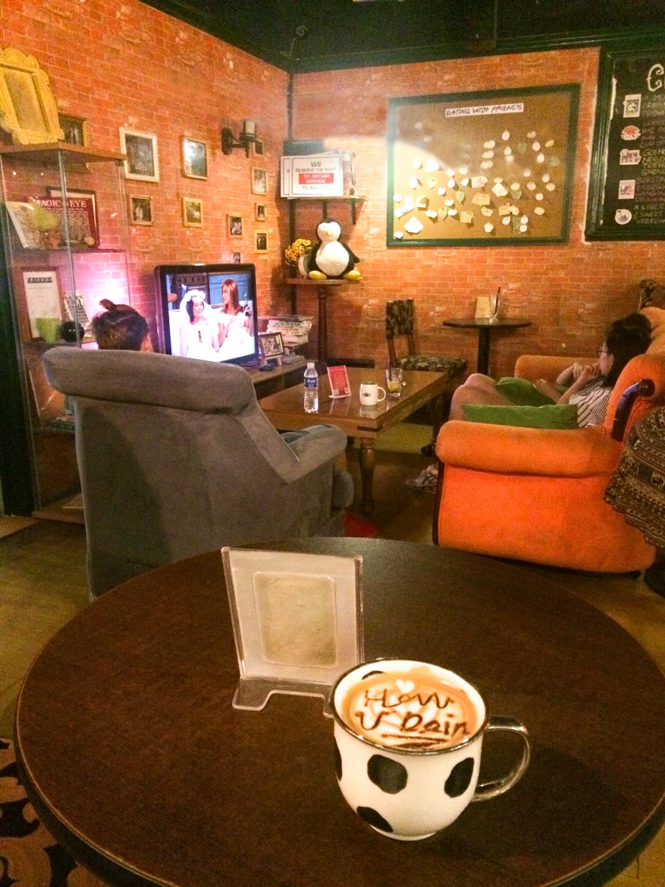 Cup of coffee with "How U Doin" written on the coffee foam on a table inside Beijing's Friends Café
