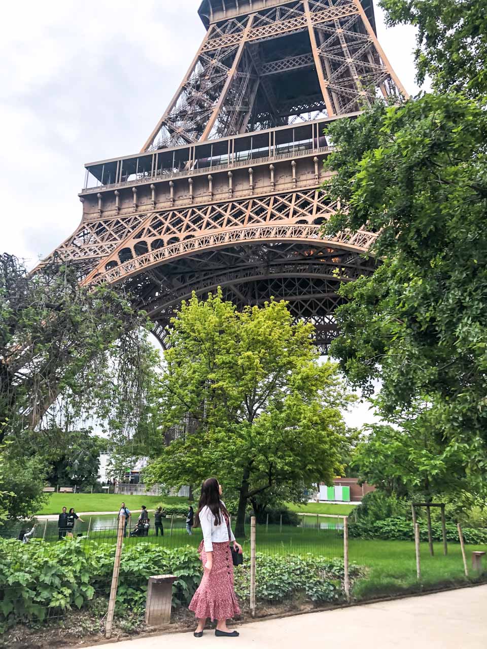 Woman in a white and red floral dress looking up at the Eiffel Tower in Paris, France