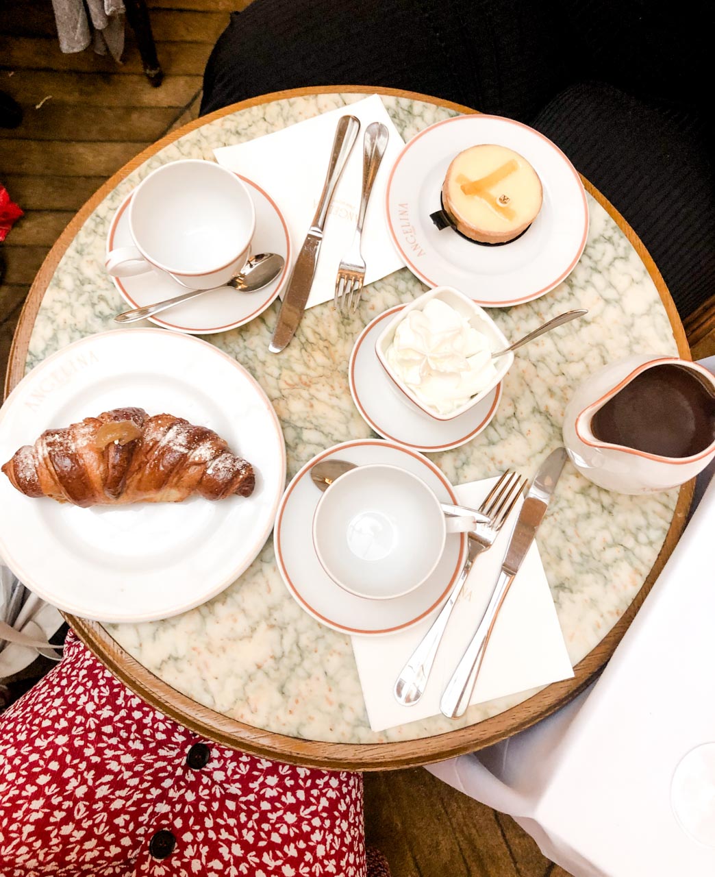 Round marble table with two cups, a lemon tart, a croissant, a pot of hot chocolate and cream