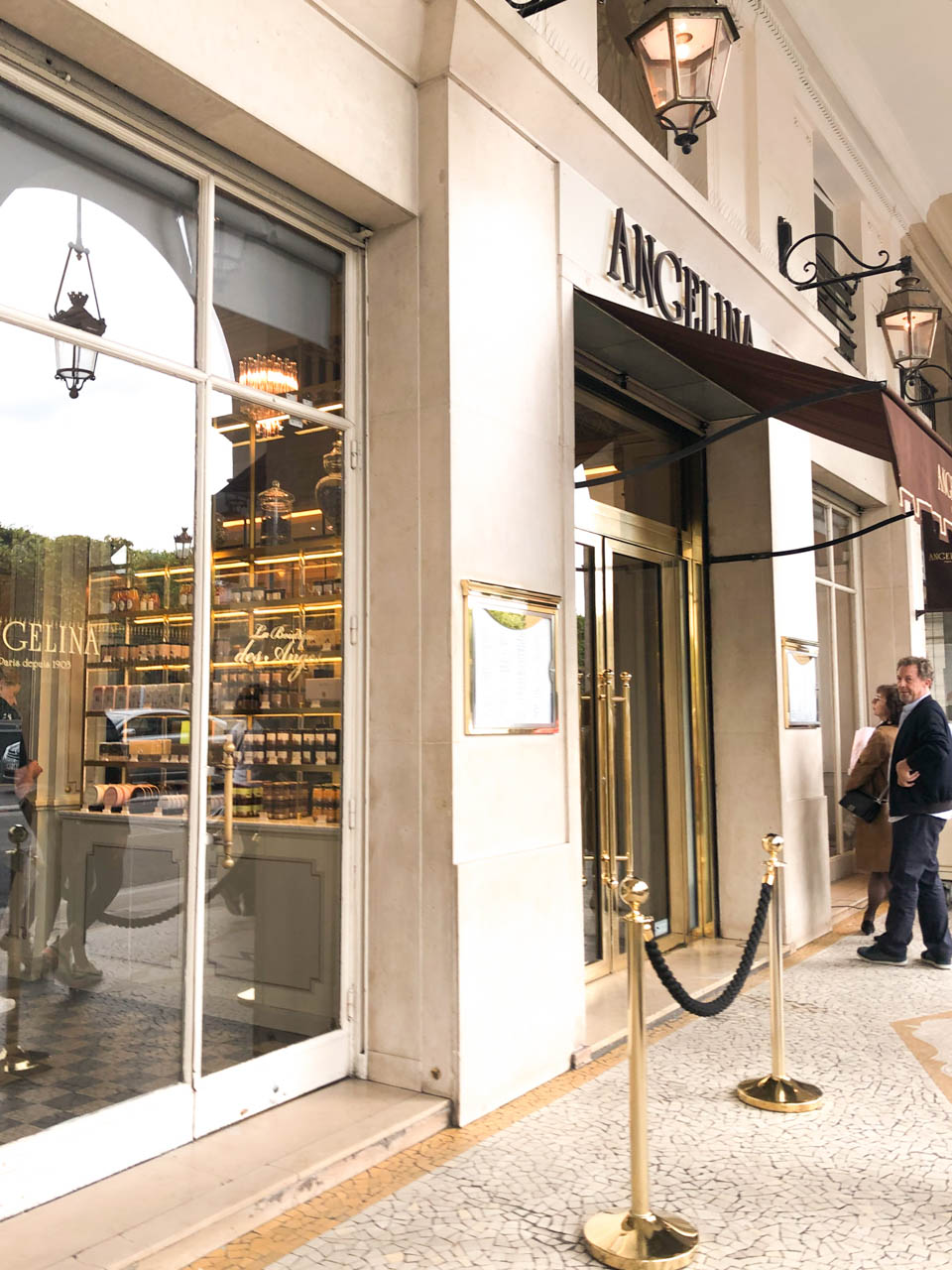 Two people standing outside the main entrance to the Angelina tea house and café in Paris