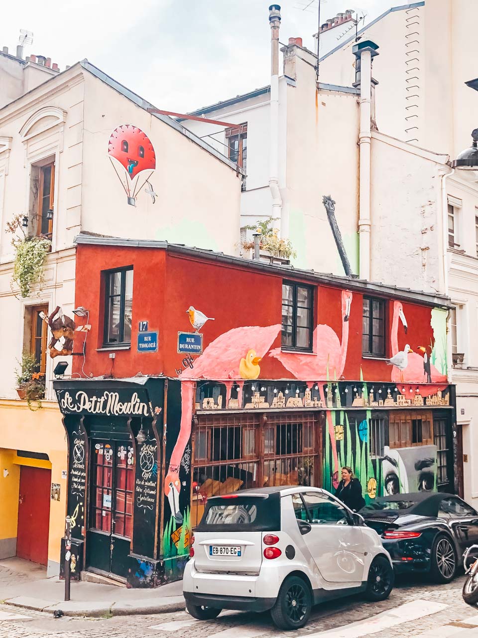 A robin, a yellow duck, and pink flamingos painted on the red façade of the Le Petit Moulin in Paris