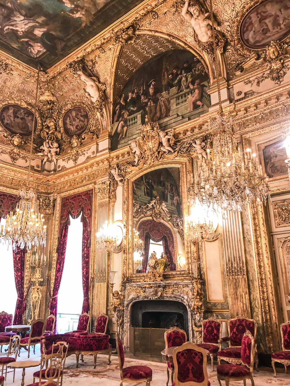 Room with gold ceilings, golden chandeliers, a fireplace and red upholstered furniture in the Louvre