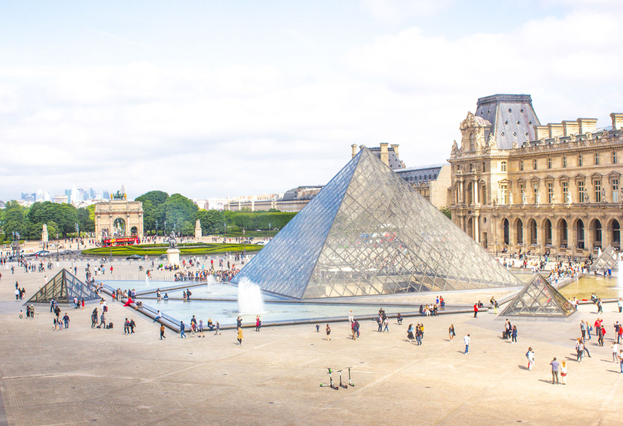 People walking around the Louvre Pyramid and a hop-on hop-off bus driving past the Arc de Triomphe