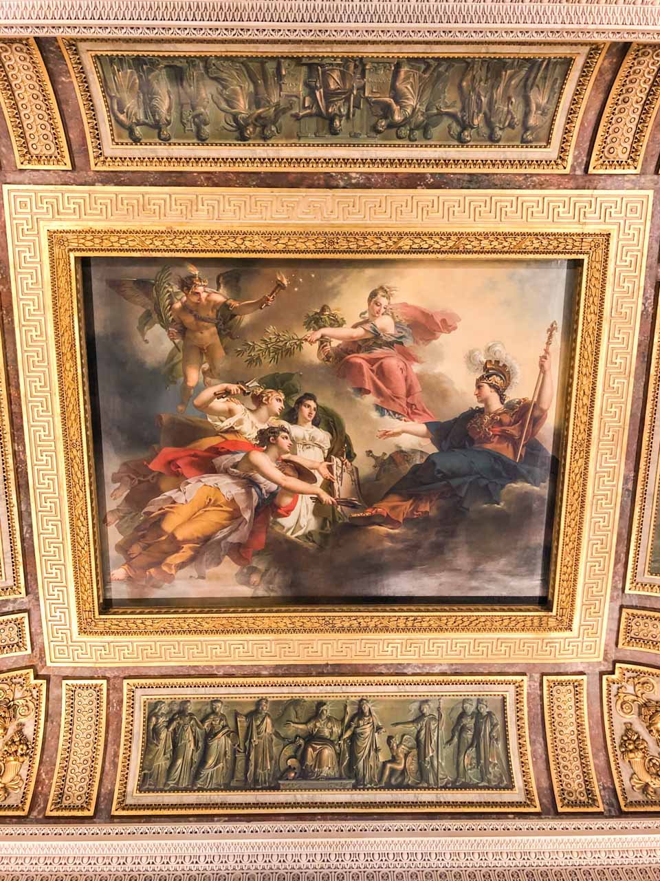 A fresco surrounded by gold edgings on the ceiling in the Louvre Museum in Paris, France