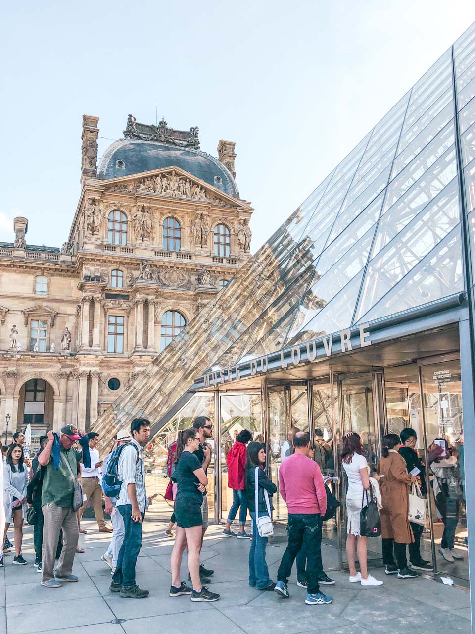 Crowds of tourists queueing outside the glass pyramid to get inside the Louvre Museum in Paris