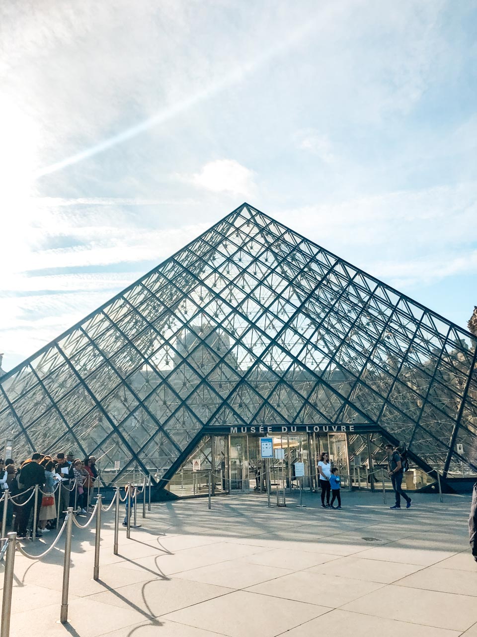 Crowds of tourists queueing outside the glass pyramid to get inside the Louvre Museum in Paris