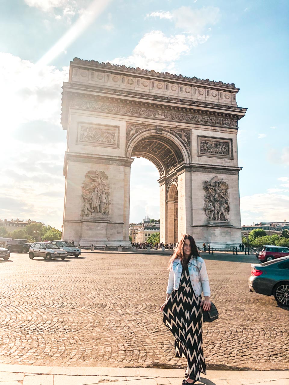 Woman in a denim jacket and a black and white maxi dress standing in front of the Arc de Triomphe