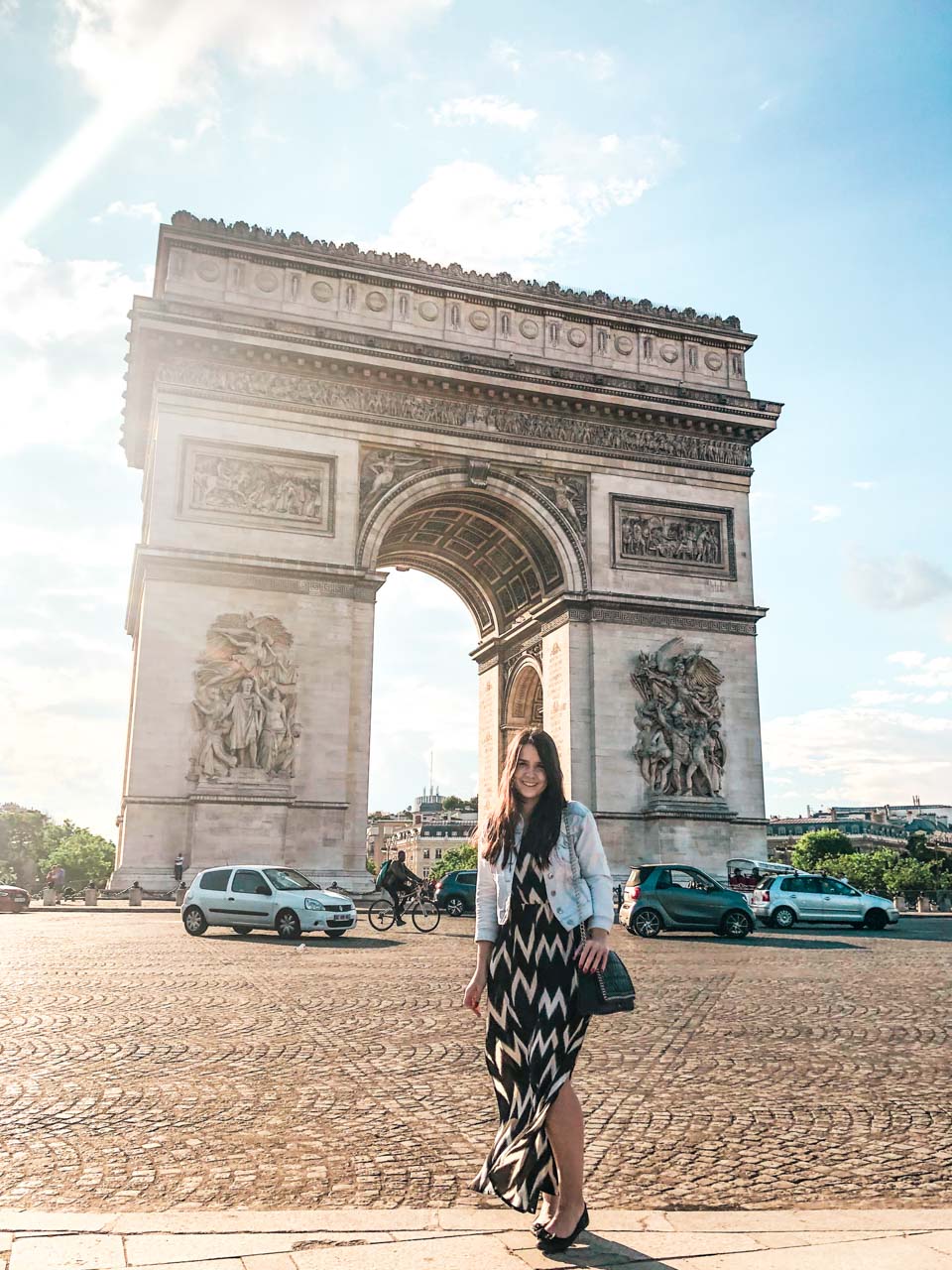 Woman in a denim jacket and a black and white maxi dress standing in front of the Arc de Triomphe