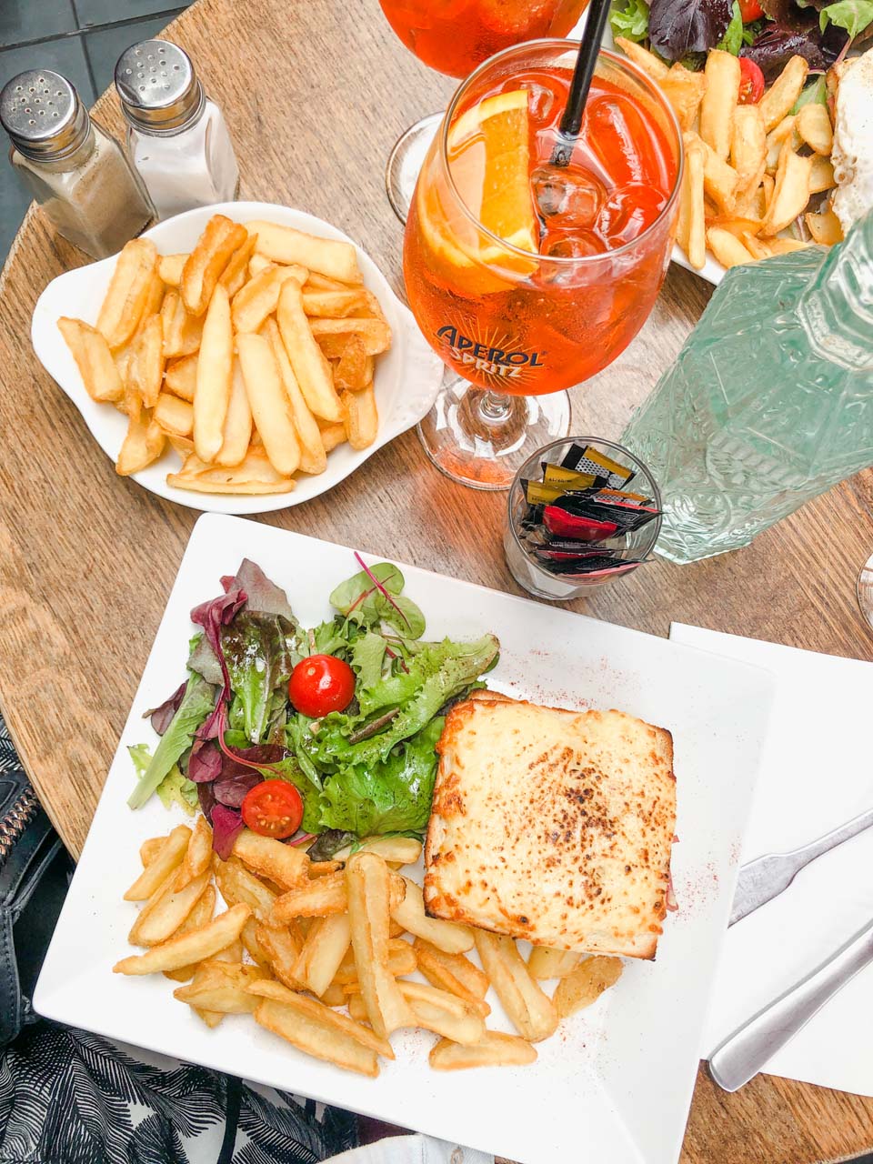 Plate of chips, a croque monsieur sandwich, a bottle of water and an Aperol Spritz on a table