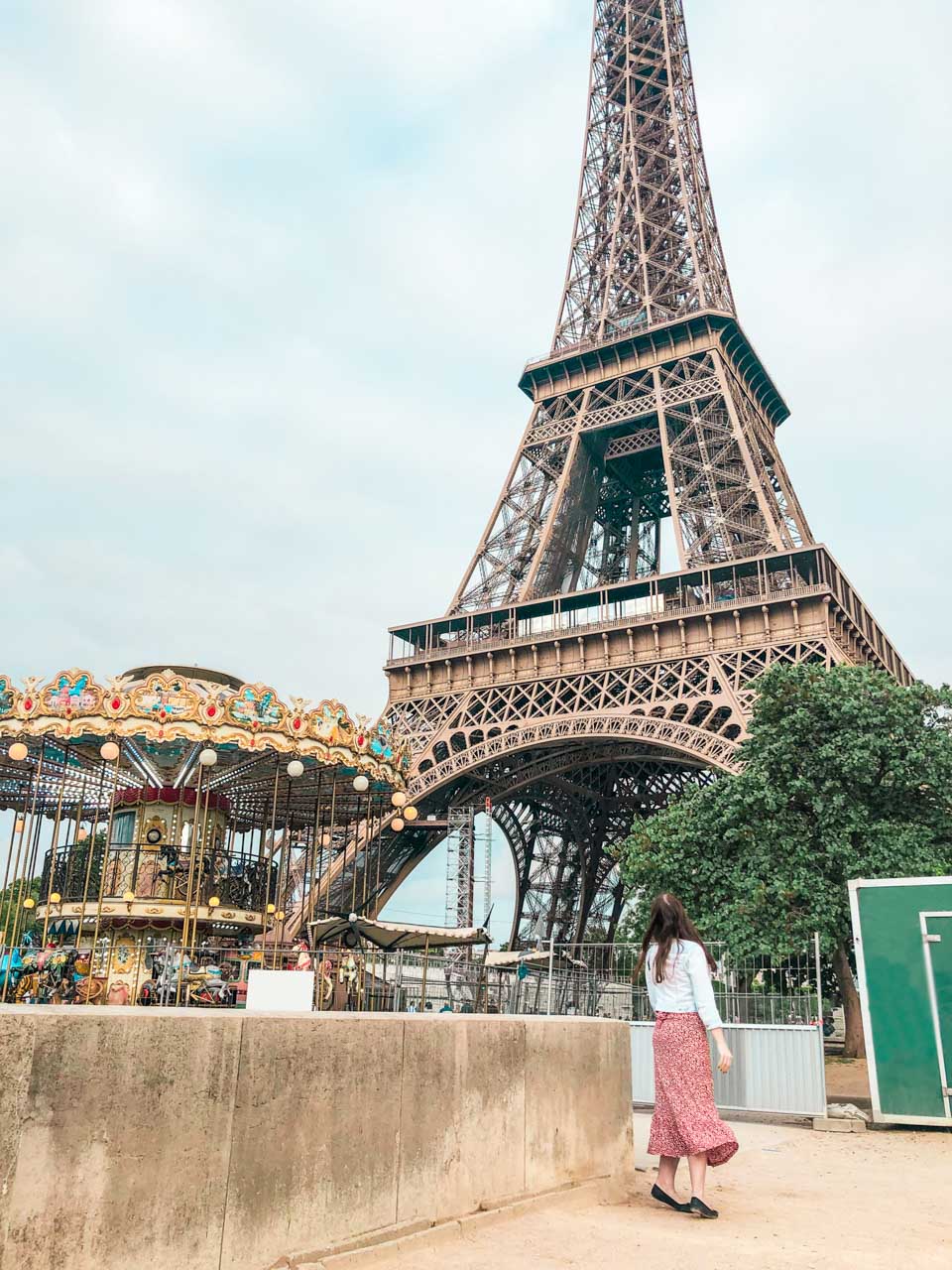 Woman in a white and red dress standing on tippy toes next to the Carousel of the Eiffel Tower