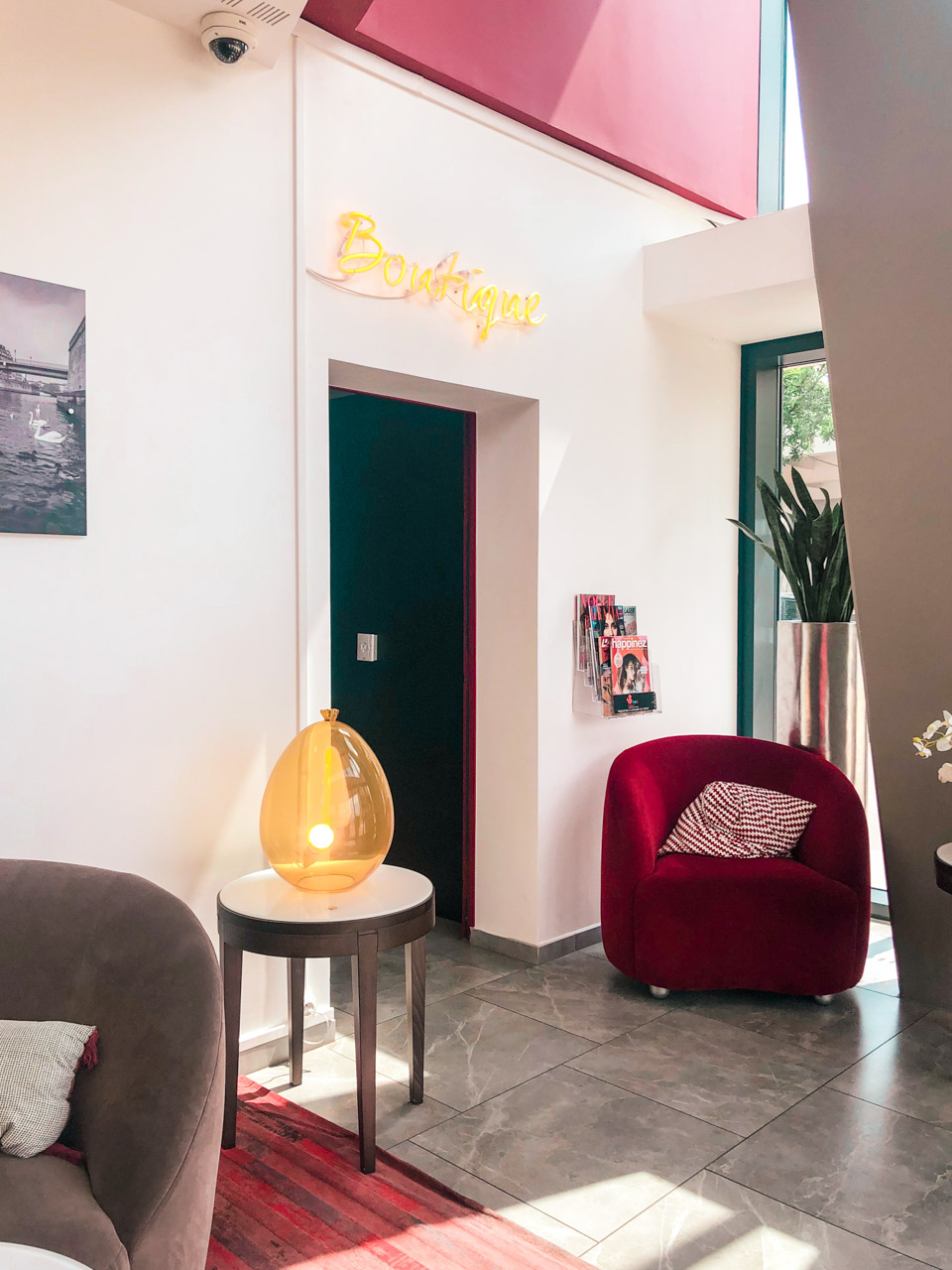 Lobby area with a red armchair, a magazine stand, and a neon sign that says 'Boutique'