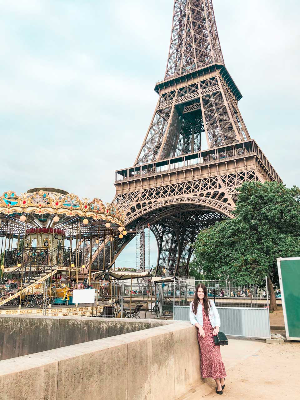 Woman in a white and red dress leaning against the ledge next to the Carousel of the Eiffel Tower