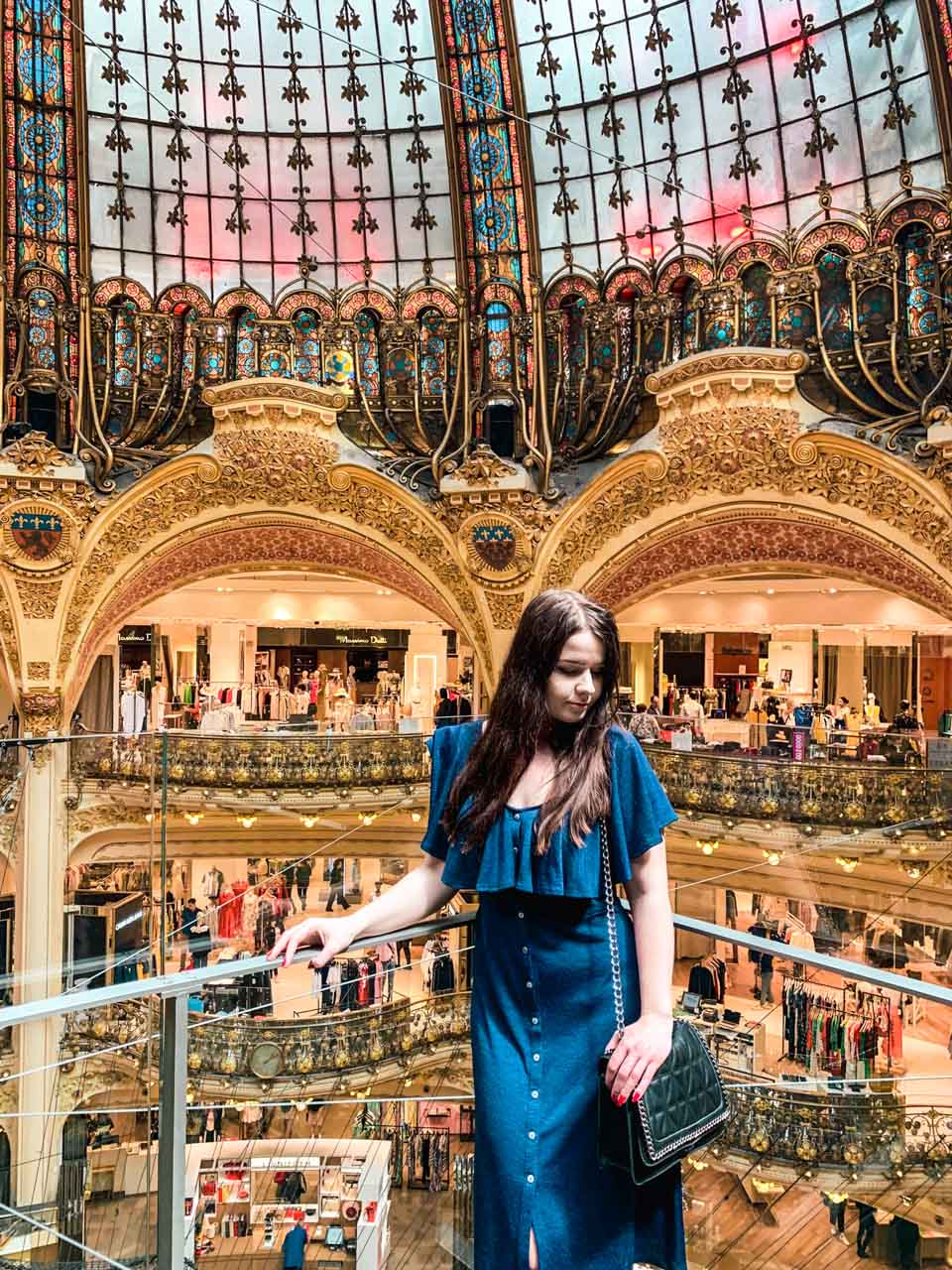 Woman in a blue dress standing on the suspended glass walkway at Galeries Lafayette Paris Haussmann