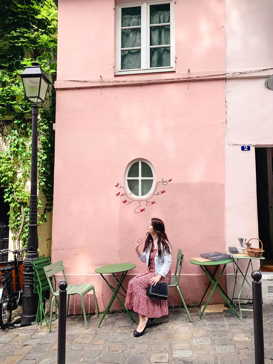 Woman in a red and white floral midi dress sitting on a chair outside La Maison Rose in Montmartre