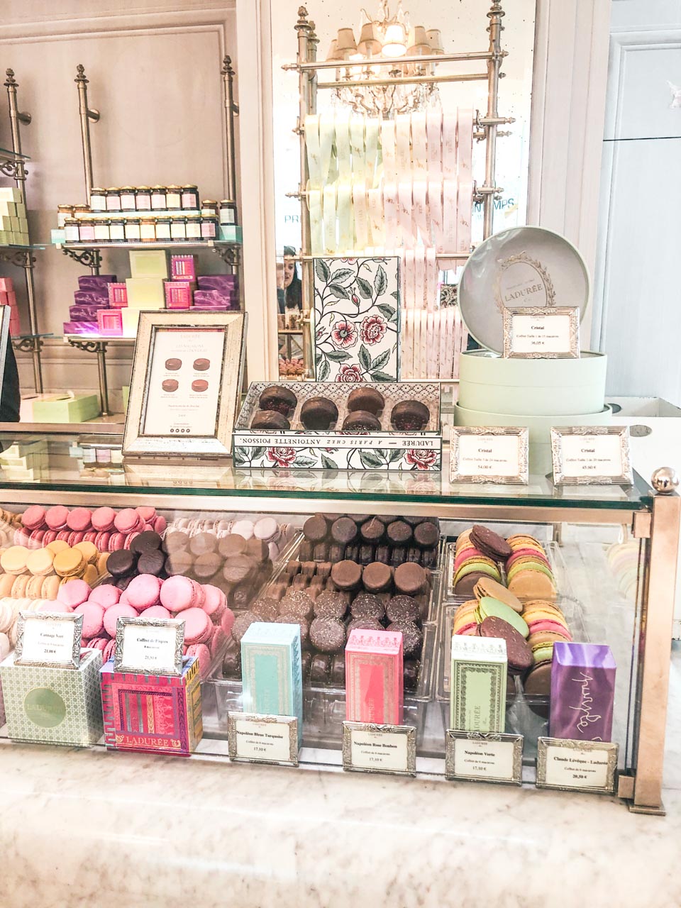 Counter area of Ladurée with macarons, pastries, and gift boxes in a glass display case