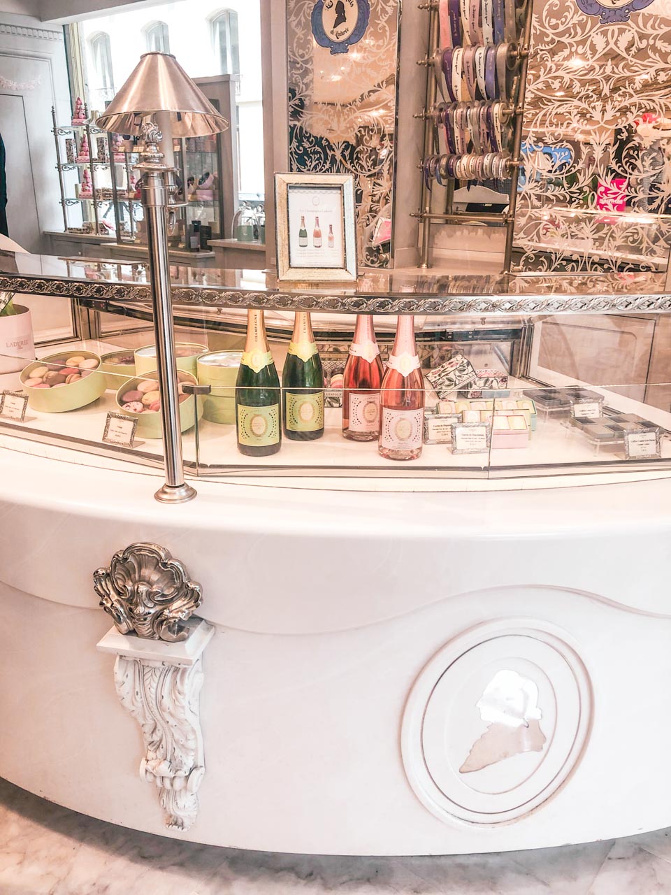 Counter area of Ladurée with macarons, pastries, and champagne bottles in a glass display case