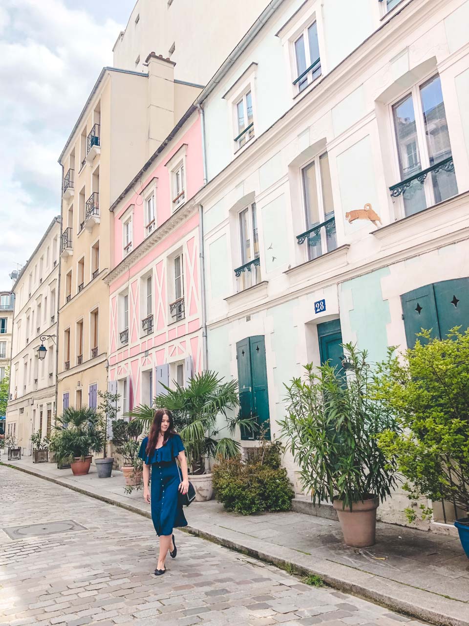 Young dark-haired woman in a blue off-the-shoulder dress walking on Rue Crémieux in Paris, France