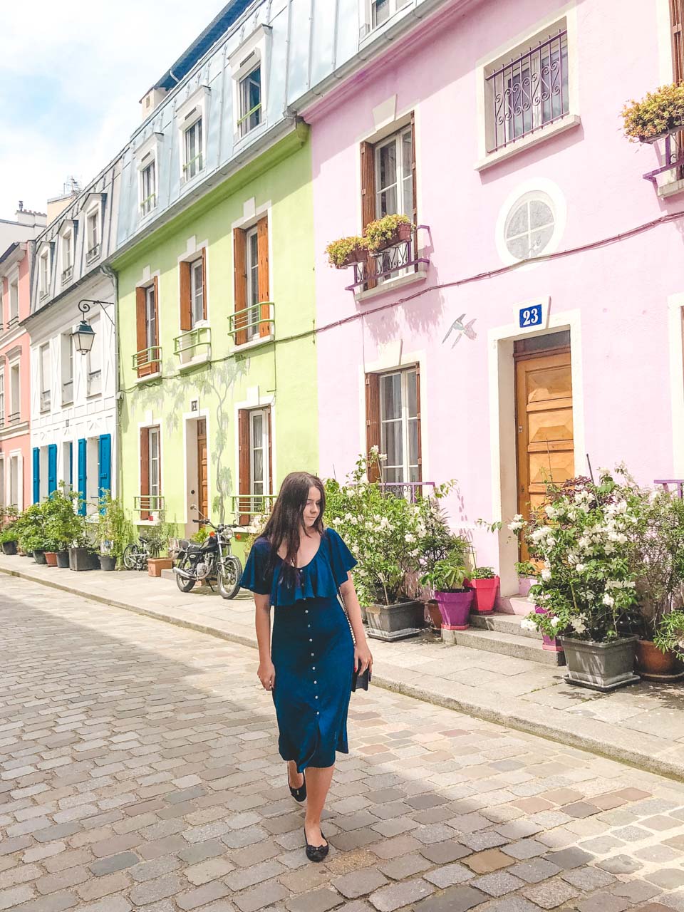 Young dark-haired woman in a blue off-the-shoulder dress walking on Rue Crémieux in Paris, France