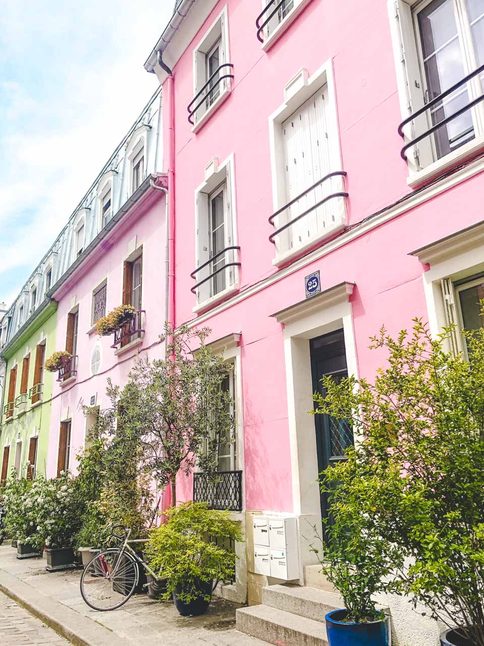 A bike parked between plant pots outside a pink house on Rue Crémieux in Paris, France